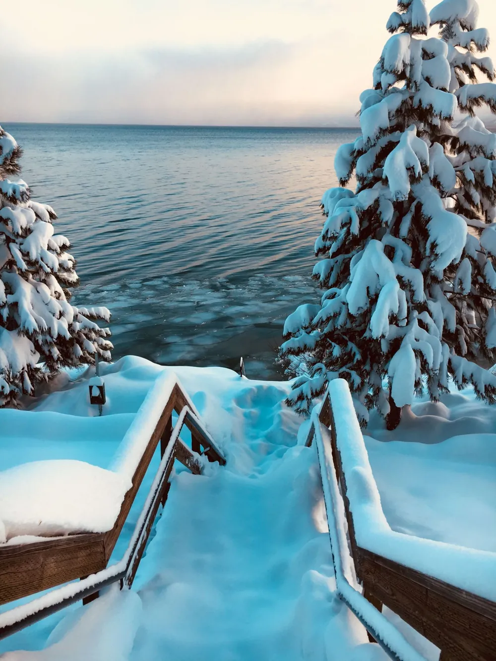 Snow-covered stairs down to a still lake between pines
